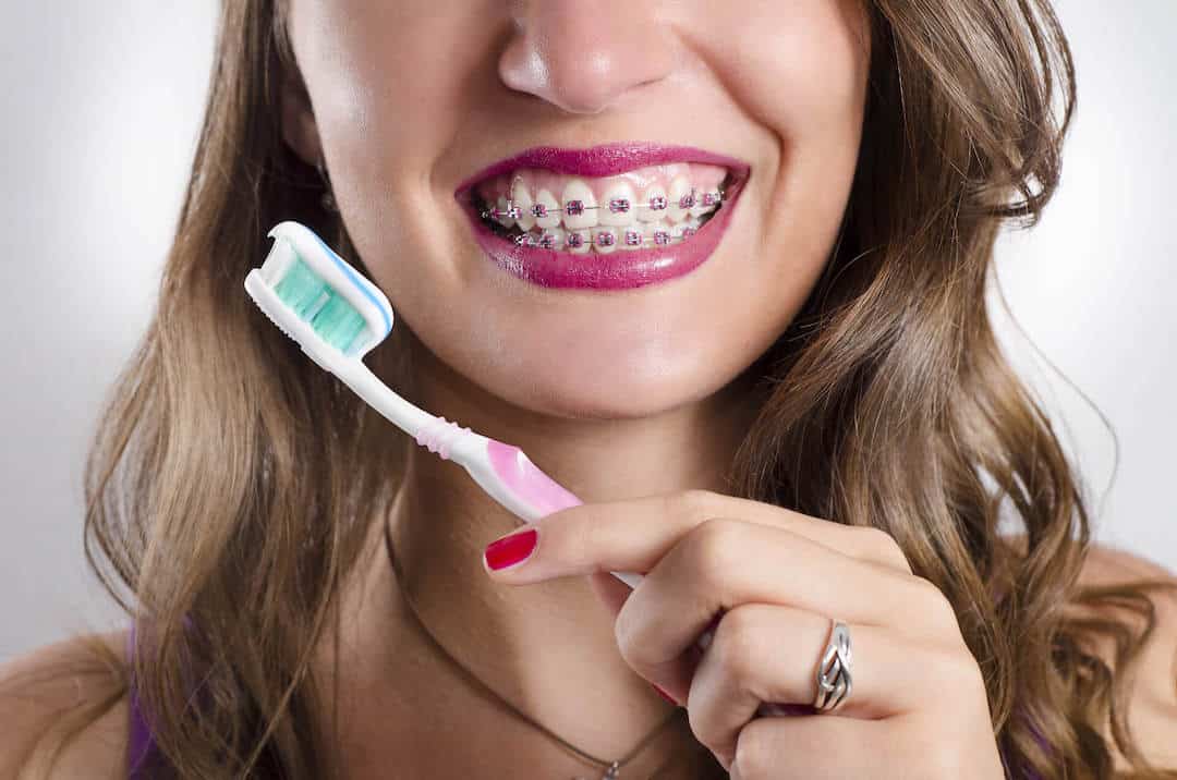 A teenage girl with braces smiles for the camera while holding a toothbrush up, ready to practice healthy dental hygiene.
