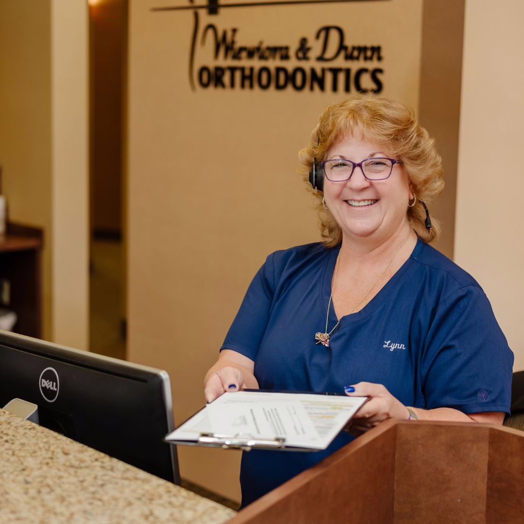 Team member at Wiewiora & Dunn Orthodontics, holding papers at front desk, smiling, Invisalign in Lake Mary and Longwood